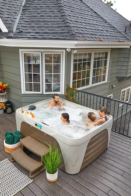 Family relaxing together in a Fantasy Spa hot tub on a backyard deck outside a home